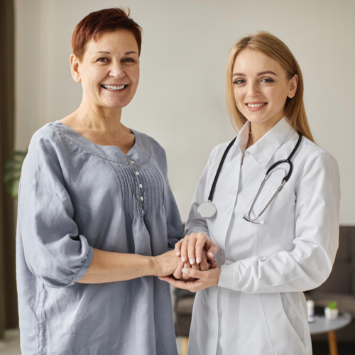 Młoda pani doktor ubrana w biały fartuch stoi razem z pacjentką.